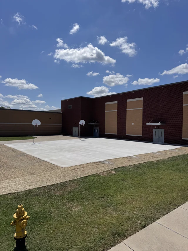 Large finished concrete surface with basketball hoops beside a brick building