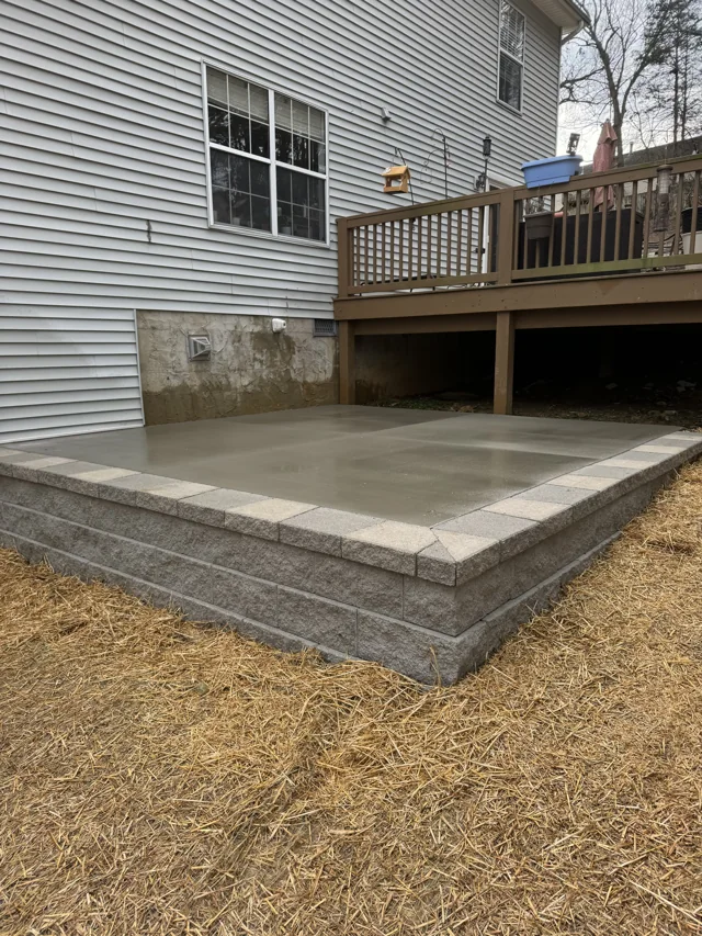 Raised concrete patio edged with a block wall underneath a deck