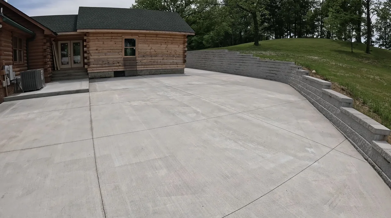 Block retaining wall following the edge of a concrete driveway beside a log home